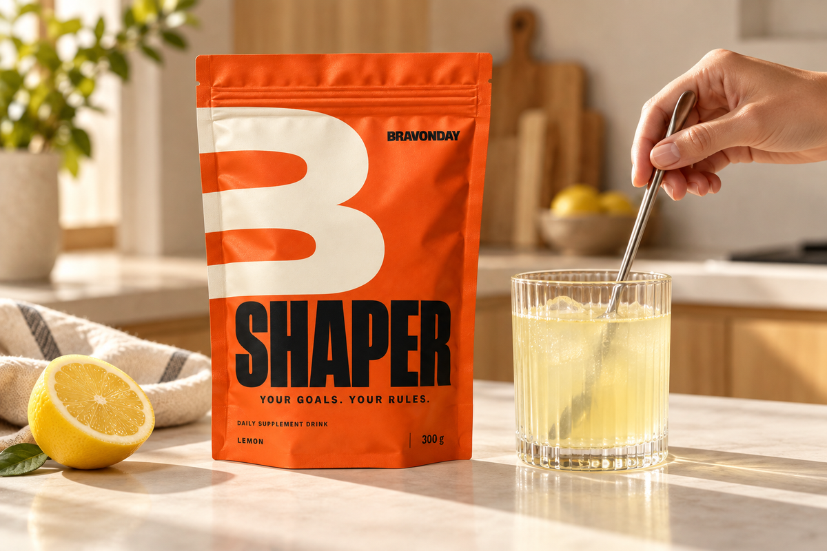 SHAPER pouch beside a hand stirring a lemon drink in a sunny kitchen.